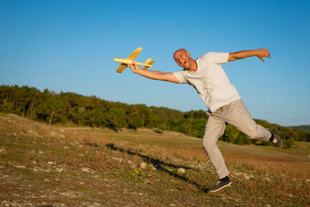 Funny bald man holding an airplane in his hand against the background of the skyの写真素材