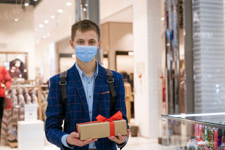 young man in a jacket holding a gift box in a store wearing a medical mask