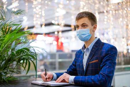 young man in a mask writes in a notebook, an employee in a shopping center