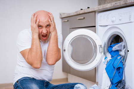 tired bald man sitting with dirty laundry in the washing machine. Cleaning conceptの写真素材