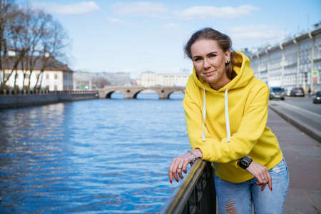 Cute young woman stands on the embankment in a yellow sweatshirtの写真素材