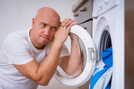 tired bald man sitting with dirty laundry in the washing machine. Cleaning conceptの写真素材