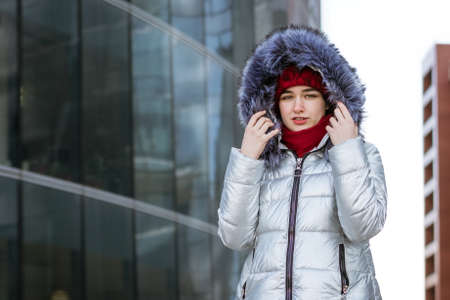 young woman in a red hat and winter gray jacket on the street posing near the building.の写真素材