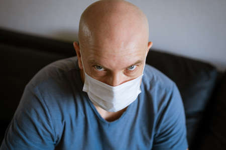 emotional portrait of a bald man in a protective mask in a blue t-shirtの写真素材