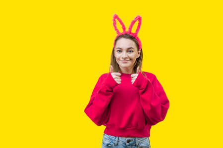 young woman, blonde, wearing pink bunny ears and a red sweater on a yellow backgroundの写真素材