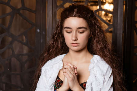 a young beautiful brunette with long loose hair in a white peignoir in the fashion of the 19th century prays - cosplay for the Broadway musical The Phantom of the Operaの写真素材