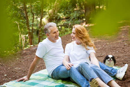 happy mature married couple in forest lie on blanket with dog, picnic conceptの写真素材