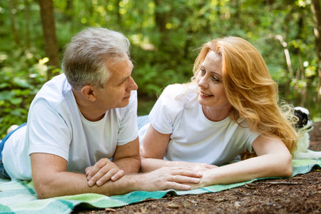 Mature adult happy couple in park hugging while sitting on plaidの写真素材