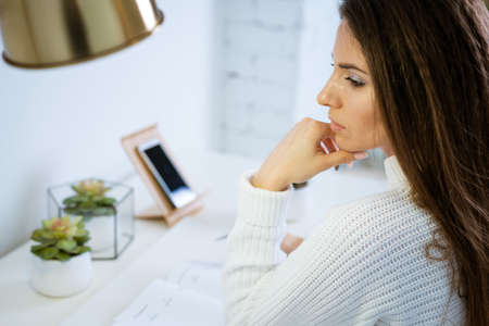 beautiful young woman in a white sweater sits at a work table with a pensive view close-up