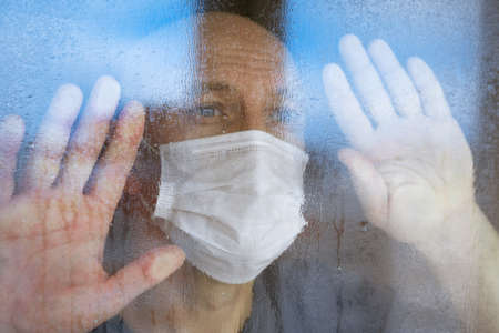 portrait of a bald man in a protective mask looking through the windows to the street close-upの写真素材