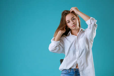 portrait of a young caucasian woman with a sad face in a white shirt on a blue backgroundの写真素材