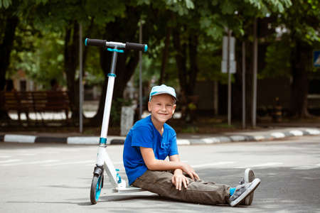 boy in a cap sits on a scooter in the park on a sunny summer dayの写真素材