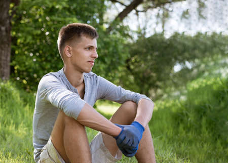 a young man voluntarily cleaned the park from garbage, sits on the grass with gloves resting after workの写真素材