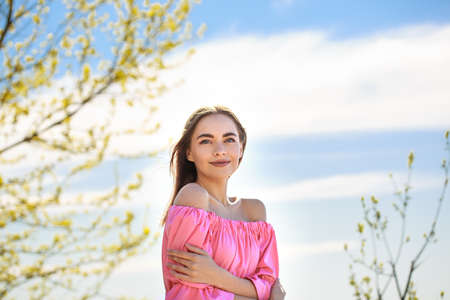 Beautiful young woman of Caucasian ethnicity with well-groomed face skin in a pink dress on a natural background, the concept of natural organic cosmeticsの写真素材
