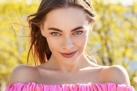 Beautiful young woman of Caucasian ethnicity with well-groomed face skin in a pink dress on a natural background, the concept of natural organic cosmeticsの写真素材