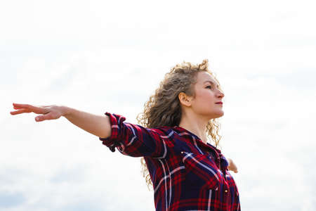 Caucasian Woman relaxing at the beach with arms open enjoying her freedom, curly hair in the windの写真素材