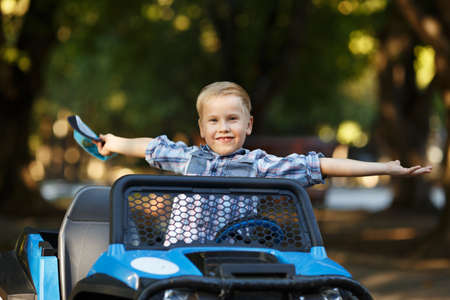 The boy plays, drives a car in the park. A cute little boy of Caucasian appearance in a cap driving a large mechanical toy truck,の写真素材