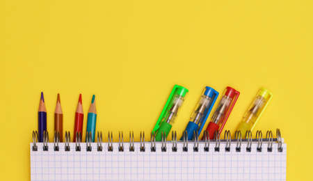 Colorful stationery is placed under a notebook on a yellow background, top view, for advertising.の写真素材