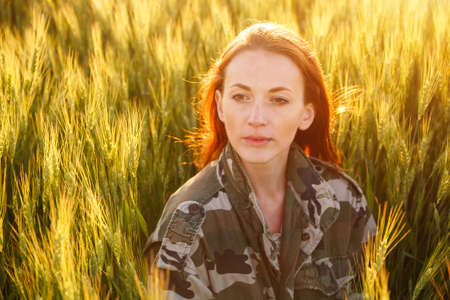 Portrait of a young happy girl sitting on a golden wheat harvest in a yellow sunset field. summer nature background. woman with red hair. young woman sitting in a wheat fieldの写真素材