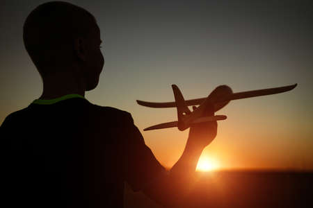 Boy throws a toy airplane in the summer at sunset. A child plays with a toy airplane, dreams of a trip. Son plays by plane in the field at sunset. Have fun and enjoy lifeの写真素材