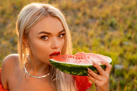 Close-up portrait of a woman biting a watermelon in nature. Beautiful girl of caucasian appearance eats a watermelon on a picnic.の写真素材