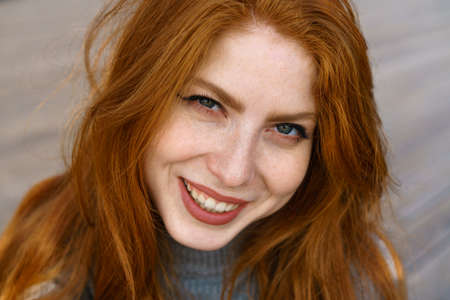 female closeup portrait, caucasian red-haired cute young woman with freckles and green eyes looks into the frame and cute smilingの写真素材
