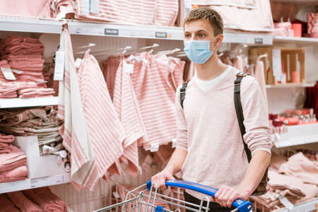 a guy of European appearance in a protective mask and casual clothes, with a trolley in the store in the department of everything for the home. Shopping during quarantineの写真素材