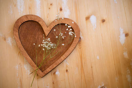 wooden heart with a sprig of small white flowers lies on a wooden backgroundの写真素材