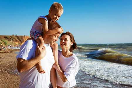 Happy family having fun on summer vacation. The son is sitting on the daddys neck. Young family on vacation have a lot of fun together.の写真素材