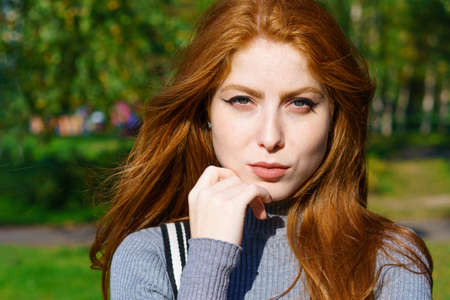 Closeup female portrait of a red-haired Caucasian woman with makeup, with green eyes looking at the...