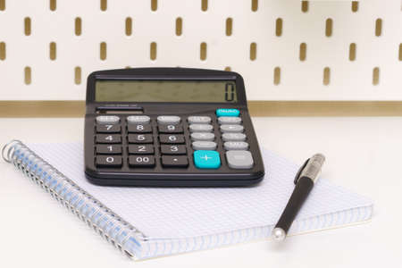 a black calculator, notepad and pen are placed on a white background of the tableの写真素材