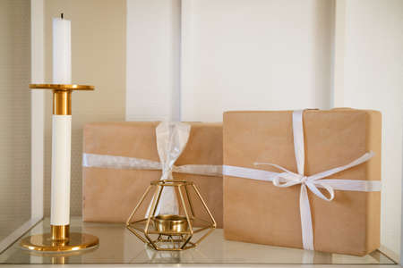 gift boxes packed with craft paper with a white bow on a shelf with a candlestick,