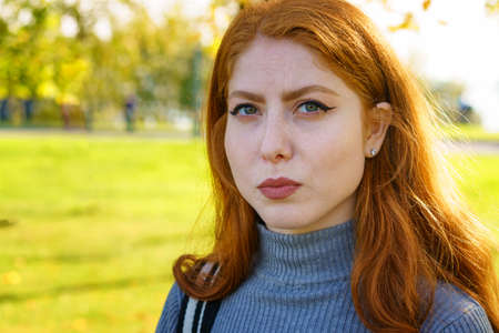Closeup female portrait of a red-haired Caucasian woman, with makeup with green eyes looking at the camera on a natural background on a sunny dayの写真素材