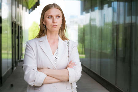 Business woman portrait Crossed arms. Happy successful professional portrait near an office building. Young caucasian business woman with clasped hands standing outside. Female business leader conceptの写真素材