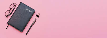 Education or business concept: top view of black notebook with modern glasses and black pen isolated on pink background.の写真素材