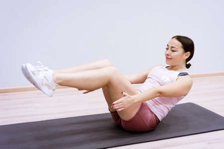A woman of Caucasian ethnicity in sportswear is engaged in fitness at home against the background of...