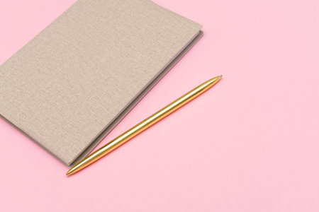 Notepad and gold pen on a pink background. Mock up, top view, copy space. Colored blocks concept.の写真素材