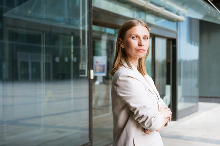 Business woman portrait Crossed arms. Happy successful professional portrait near an office building. Young caucasian business woman with clasped hands standing outside. Female business leader conceptの写真素材