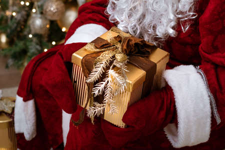 Santa Claus holds a gift in mittens on a Christmas tree, festive mood