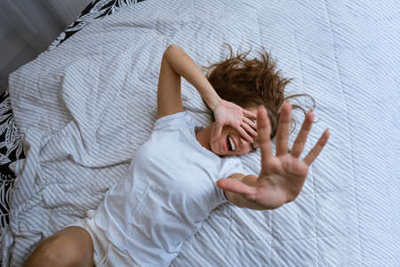 Overjoyed woman in pajamas stretching out her arms after waking up lying in cozy bed, happy smiling attractive young woman starting new day enjoying the morning after a healthy sleep, doing exercisesの写真素材