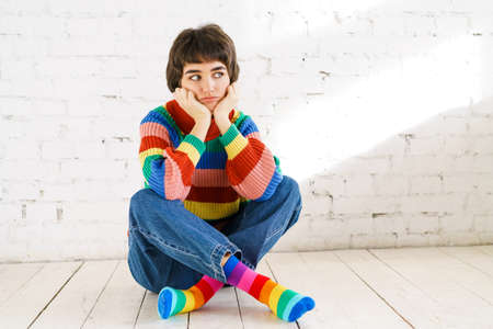 Photo of young sad beautiful girl thinks that dream was surprised, touching her hand to her face looks like empty space, against the background of a white brick wallの写真素材