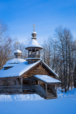 a snow-covered, ancient, wooden church among the trees against the blue sky. winter sunny dayの写真素材