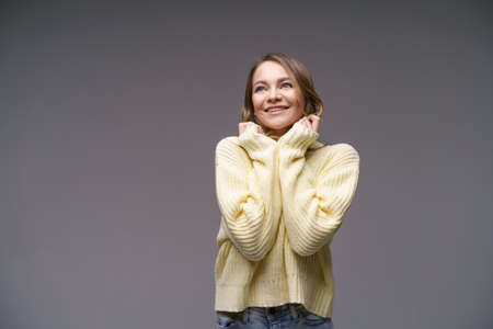 Portrait of a beautiful young girl of Caucasian ethnicity in a yellow sweater on a gray background...