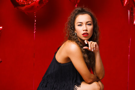 Funny girl with red balloons on a red background. Young woman festive mood with balloons in the form...