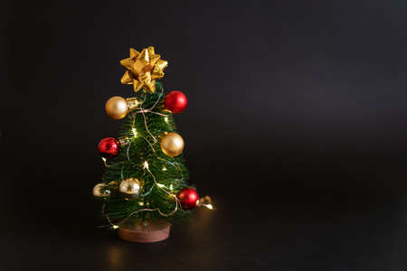 Toy christmas tree with balls on a black background with a garland. Cute holiday decor in a dark style.の写真素材