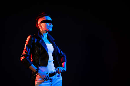 Night portrait of woman. Neon light. Positive attitude. Confident happy woman, wearing leather jacket and sunglasses, smiling in red blue glow isolated on black backgroundの写真素材