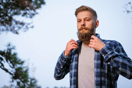 Young caucasian bearded man in plaid shirt traveling alone in autumn forest and looking to the side. Hiking, outdoor travel, recreation and active adventure conceptの写真素材