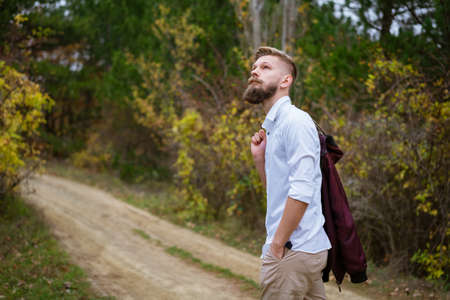 Portrait of a young bearded man walking on the road in the park in autumn. Handsome caucasian man in...