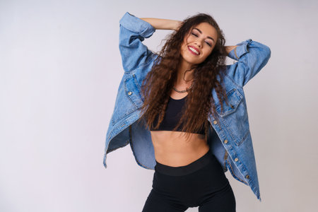 Happy cheerful young woman rejoicing at positive news or birthday present smiling with snow white smile. Caucasian girl with curly hair cheerfully posing in a denim jacket on the backgroundの写真素材