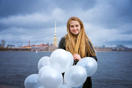 Happy cheerful girl having fun with big white latex balloons. Outdoors on the waterfront by the...